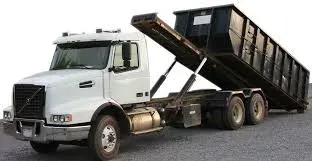 White Volvo roll-off truck tipping a black roll-off container at a job site